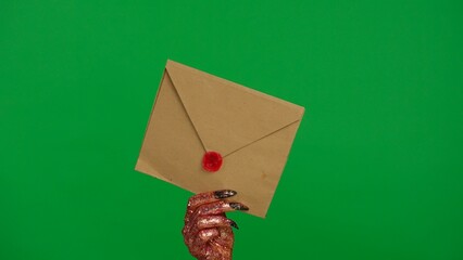 Obraz premium Creepy halloween monster human hand in glitter slime with nails holds antique envelope, isolated on chroma key green screen background, workspace mockup.