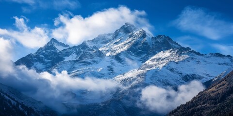 Obraz premium A breathtaking view of snow-covered mountains shrouded in clouds, juxtaposed with a vibrant blue sky, showcasing nature's grandeur.