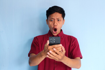 Young Asian man looking his mobile phone with shocked expression