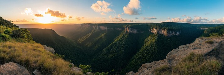A beautiful landscape with a mountain range and a valley. The sun is setting, casting a warm glow over the scene. The sky is filled with clouds, creating a serene and peaceful atmosphere