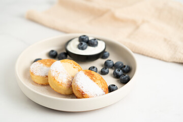 Healthy breakfast, homemade traditional cottage cheese pancakes syrniki with berries and cream on a light background.