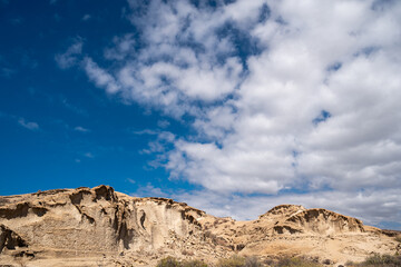 A mountain range with a blue sky in the background. The sky is partly cloudy, but the sun is still shining through. The mountains are rocky and barren, with no vegetation in sight