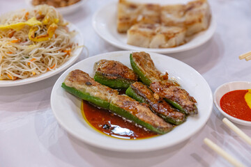 Close-up of stuffed bell peppers in a savory brown sauce, served alongside stir-fried noodles, creating a flavorful Chinese dim sum meal.
