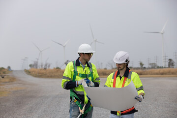 Male engineer at windmill field farm, wearing safety uniform and working nd inspecting quality of...