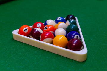 Detailed shot of colorful billiard pool balls arranged in a triangle rack on a green felt table, snooker cue ball visible in the background