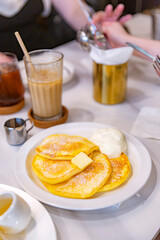 ight and fluffy souffle pancakes with a golden brown finish, served with whipped cream and syrup, presented beautifully on a white plate at a cafe
