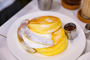 Close-up of fluffy souffle pancakes topped with powdered sugar and served with whipped cream,...