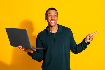 Photo portrait of handsome young guy netbook point look empty space dressed stylish green garment isolated on yellow color background