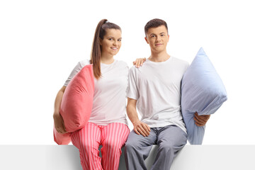 Young couple in pajamas posing in embrace seated on a panel
