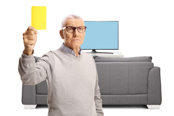 Serious elderly man showing a yellow card in front of tv