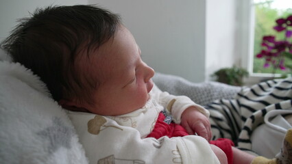 Close-up of baby resting on soft blanket, gazing calmly, natural light from a nearby window...