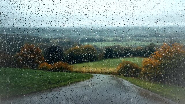 Rainy autumn day view of a winding road and countryside seen through a water-dotted window. Nature concept