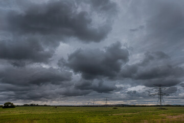 High voltage overhead power line. Green meadow with a cloudy stormy sky