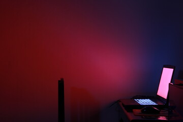 Naklejka premium Red and Blue Gradient Workstation: An abstract, minimalist image featuring a laptop and desktop computer in a dimly lit room with a red and blue gradient wall. The image evokes a sense of focus and co