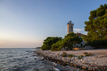 Beautiful sunset in a landscape on a rocky coast with a striking lighthouse and pine forest. View over the coast to the building, on the Mediterranean, Vir, Dalmazien, Croatia, Adriatic