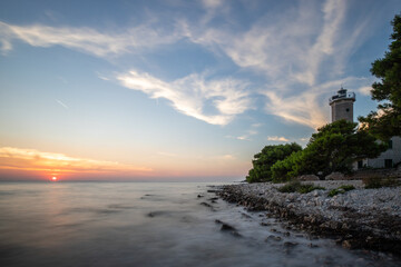 Beautiful sunset in a landscape on a rocky coast with a striking lighthouse and pine forest. View over the coast to the building, on the Mediterranean, Vir, Dalmazien, Croatia, Adriatic