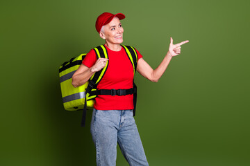 Photo of pretty senior lady delivery employee thermo bag point look empty space wear red uniform workwear isolated on khaki background