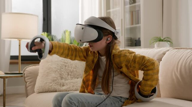 Curious Caucasian child girl little kid wear virtual reality headset vr gear wireless device. Schoolgirl daughter use controllers playing 3d video game in metaverse cyberspace world online home couch