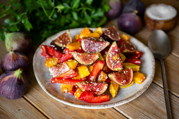 Salad with figs, tomatoes, sweet peppers and sesame seeds on a white plate on a wooden table. Salad with figs and vegetables on the table. Close-up