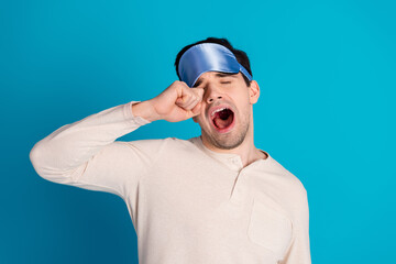 Photo of nice young man yawn rub eye wear pajama isolated on blue color background
