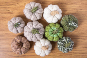 Knitted white, green and beige pumpkins on brown wooden background with place for text. Concept of autumn, Halloween, Thanksgiving. Handmade work. Flat lay, copy space