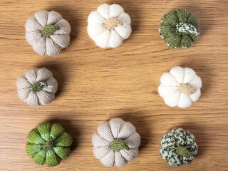 Knitted white, green and beige pumpkins on brown wooden background with place for text. Concept of autumn, Halloween, Thanksgiving. Handmade work. Flat lay, copy space