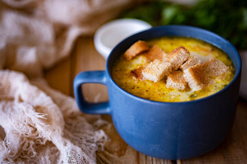 Hearty lunch: onion soup with cheese and crackers in a beautiful plate on a wooden table. Cheese soup in a blue plate with croutons. Close-up.