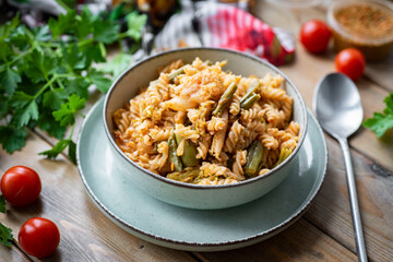 Hearty lunch: pasta with vegetables in a plate on a wooden table. Vegetarian dish.
