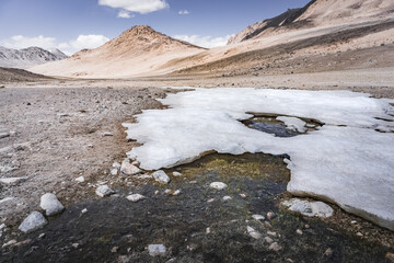 Snow in the mountains melts and streams flow from it against the backdrop of the rocky Tien Shan mountains in Pamir in Tajikistan, landscape for the background