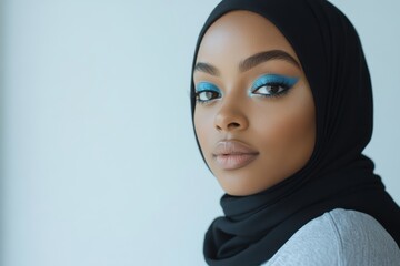 Naklejka premium A confident woman showcases her bold blue eye makeup while wearing a stylish hijab, creating an elegant and modern look