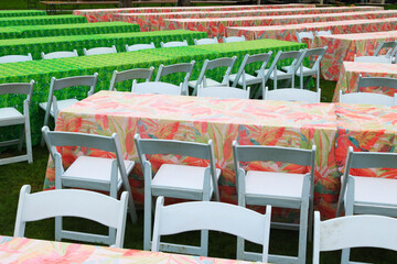 Colorful table and folding chair rows lined up in preparation for a big outdoor dinner event on...
