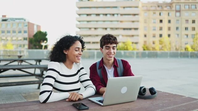 Young multi-ethnic students studying together on a laptop computer sitting on a bench on a university campus. Preparing for final exams. Concept of education and technology