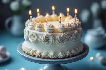Beautiful white birthday cake with floral decorations and candles on a blue table, ready for celebration at a joyful occasion