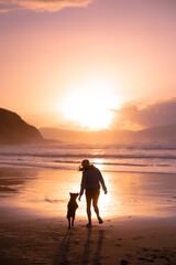 Obraz premium puppy running and a woman on the beach at sunset in the Basque Country