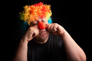 Adult man with wig and clown nose, selective focus, dark background.