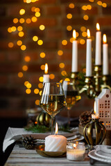 Luxury elegant Christmas dinner table setting with old vintage golden chandelier, candles, fir tree branches, wooden furniture. Porcelain houses as centrepiece, garland with lights on background