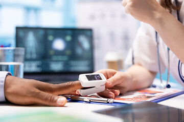 Fototapeta premium Physician specialist placing an oximeter on patient finger to take oxygen levels and saturation measurement, monitoring pulse and vital signs. Professional medic consults on health insurance.