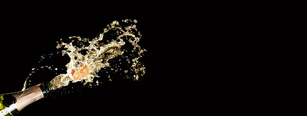 Holiday, birthday, New Year, anniversary or Christmas celebration theme. Explosion of splashing champagne sparkling wine with popping cork out on black background. Free space