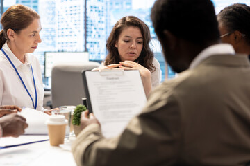 Diverse team of business people meeting in boardroom to examine annual records, looking over sales infographics to improve the services for global development. Enterprise staff.