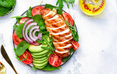 Grilled chicken fillet with avocado, spinach and tomato garnish, white background, top view