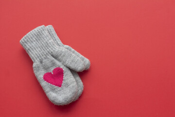 A pair of gray wool mittens with red hearts on a red background with copy space. Valentine's Day concept 