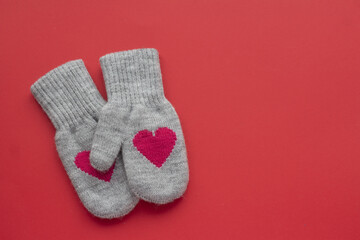 A pair of gray wool mittens with red hearts on a red background with copy space. Valentine's Day concept 