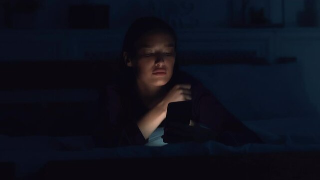 Sleep disorder. Young woman networking on cellphone, can't sleep late at night, lying in bed
