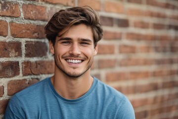 Obraz premium Attractive young man outdoors smiling and looking in camera blue shirt in front of brick wall