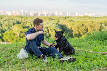 Caucasian man sitting with pit bull terrier on green lawn. 