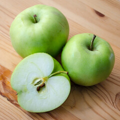 Three Earligold apples on a wood surface, including one cut in half to show the interior