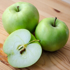 Three Earligold apples on a wood surface, including one cut in half to show the interior