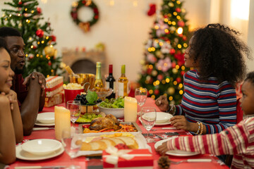 family moment during Christmas as they exchange gifts around festive dinner table. The table with Christmas-themed tableware, candles and delicious food. The room is adorned with holiday decorations.