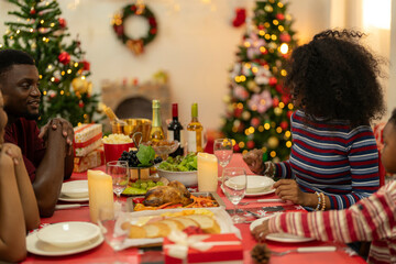 family moment during Christmas as they exchange gifts around festive dinner table. The table with Christmas-themed tableware, candles and delicious food. The room is adorned with holiday decorations.