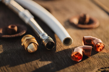 Plumbing parts lying on a rustic wooden table on a sunny day. PEX pipe, hose and brass nipple...